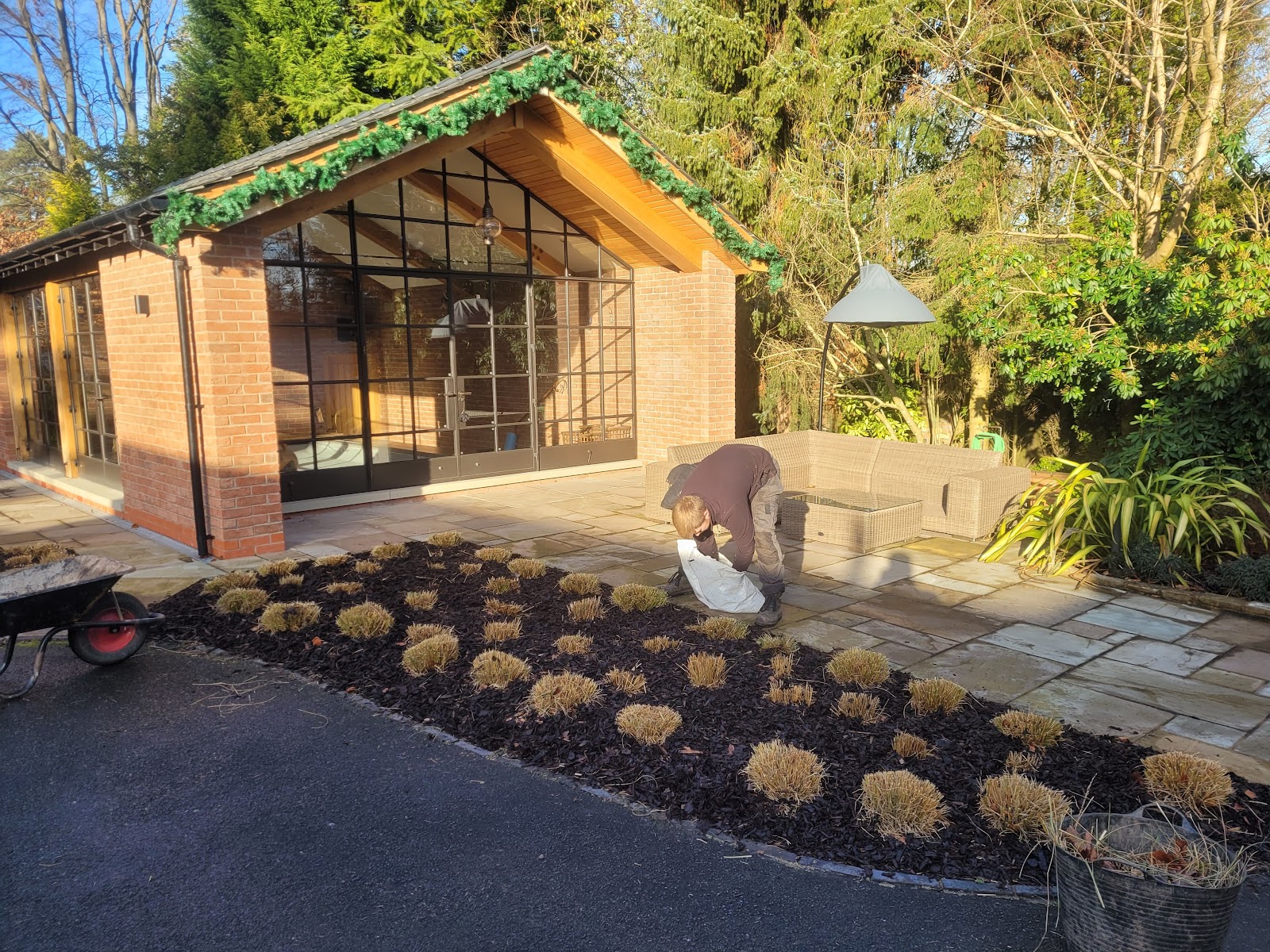 A new planting bed of ornamental grasses laid out on fresh mulch beside a paved terrace and garden room.